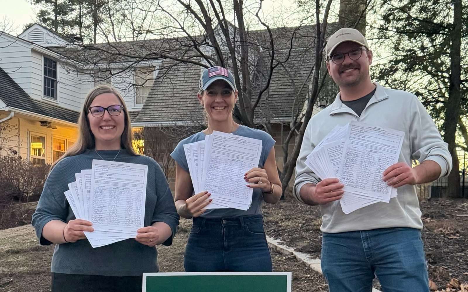 Three Victory Field Operations team members standing outside holding completed petition sheets after a day of field collection.